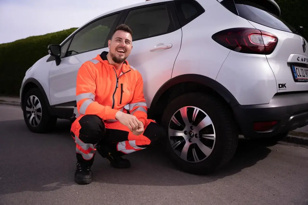Autoredder sidder på huk foran bagdæk på bil og smiler