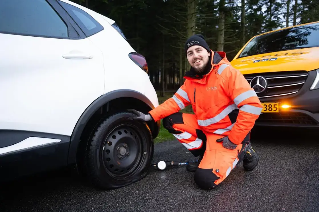 Autoredder sidder ved dæk med dæktryksmåler