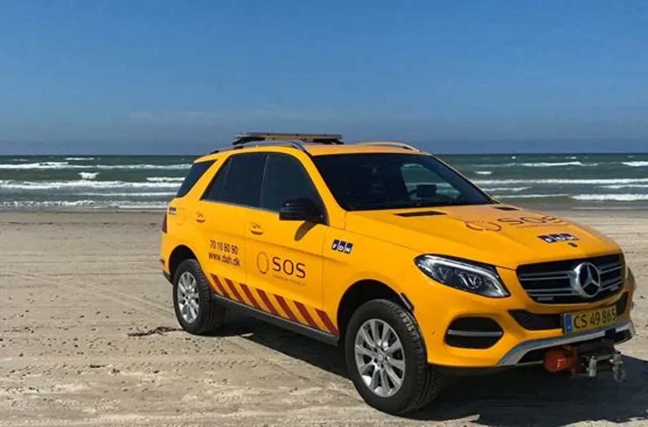Autoredder bil ses på strand. Billedet taget forfra hvor man ser passagersiden af bilen. I baggrunden ses havet. 