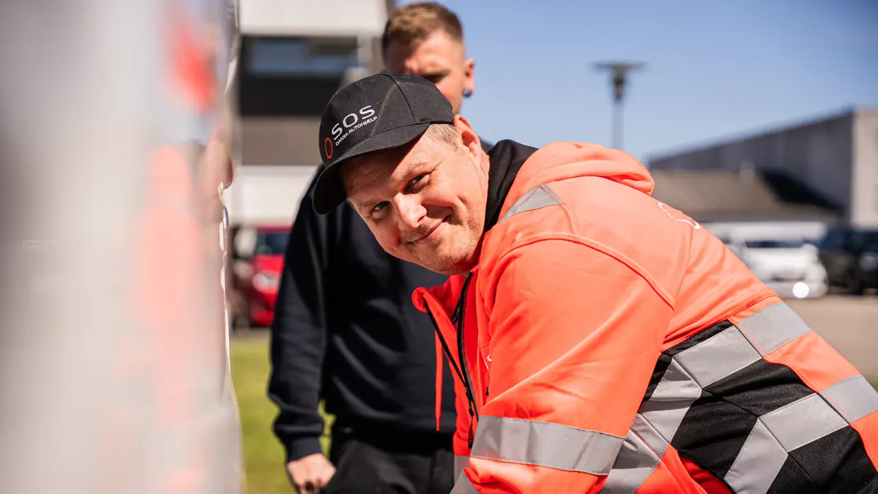 Autoredder smiler til kamera ved siden af lastbil