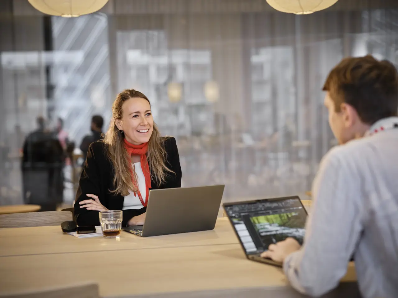 Kvinne som smiler sittende ved et bord – foran en mann med PC