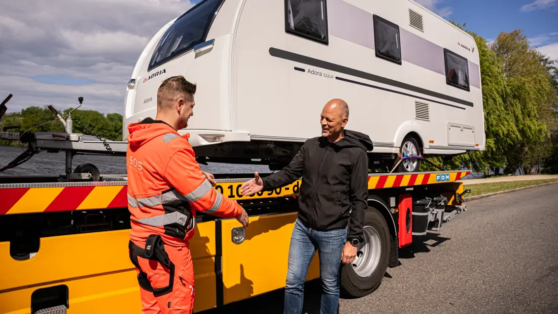 Autoredder og ejer af campingvogn giver hånd. Campingvogn på lad. 