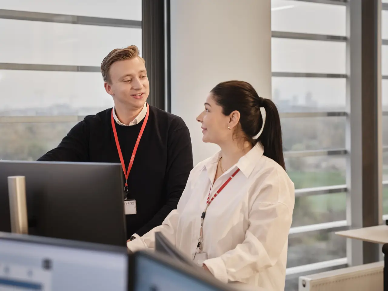 Mand og kvinde står foran PC i åben og lyst kontor