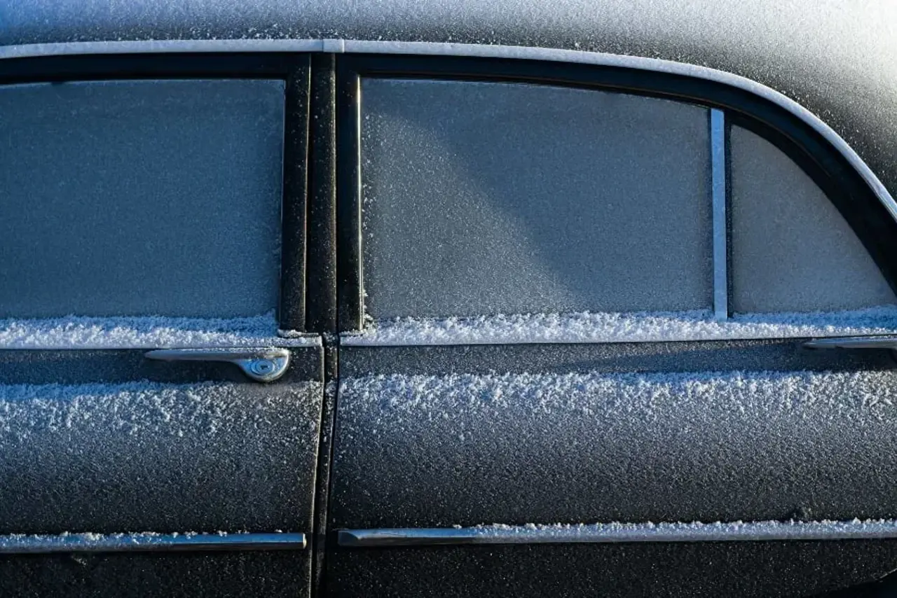 Närbild på bildörrarna av en svart bil. Dörrarna, fönsterna och tacket är täckt av frost. Bilen har silvriga lister längst bildörrarna silvrig handtag.