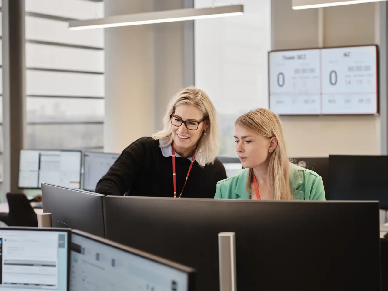 To kvinder i en alarmcentral kigger på skærm og smiler