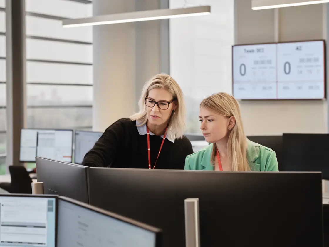 to kvinder på alarmcentral foran computere peger på skærm