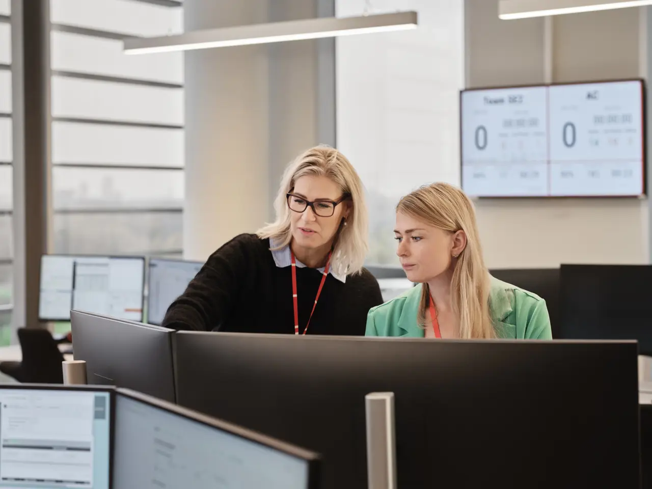 to kvinder på alarmcentral foran computere peger på skærm