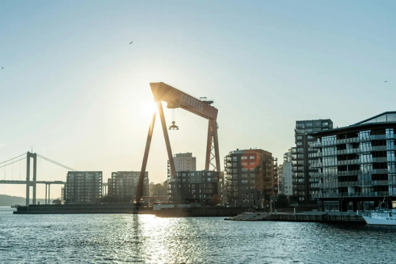 Den röda Eriksbergskranen i Göteborg mot en ljus solnedgång vid vattnet.