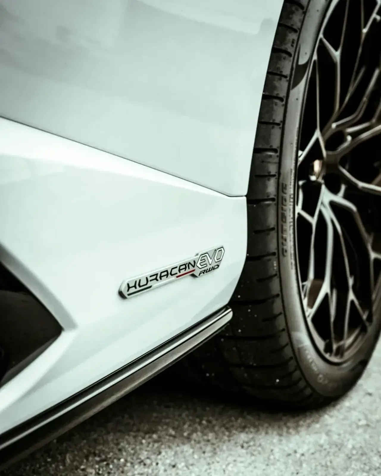 Närbild på däcket av en vit bil med svarta fälgar som står stilla på en asfaltsväg.