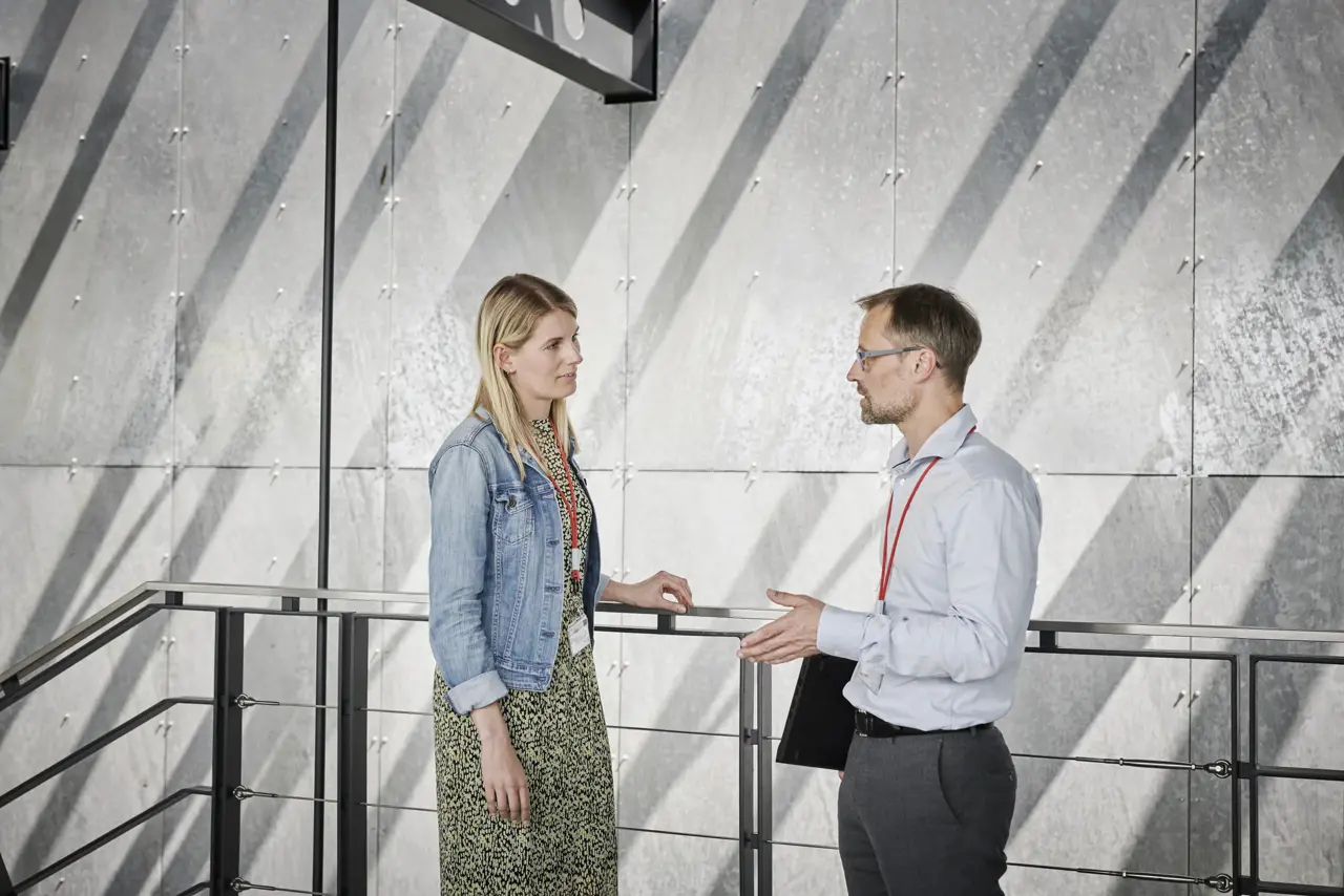 To personer står ved en trapp. Damen i kjole og mannen i skjorte.