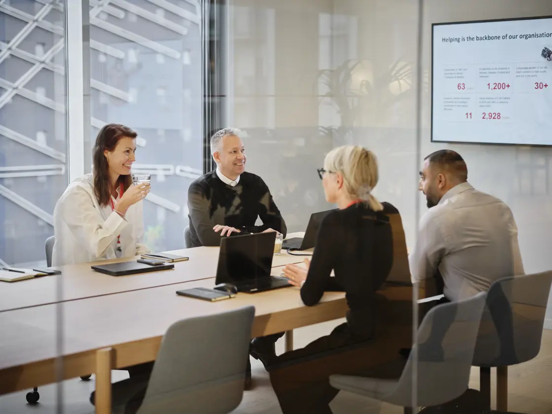 Fire personer sidder ved bord i mødelokale