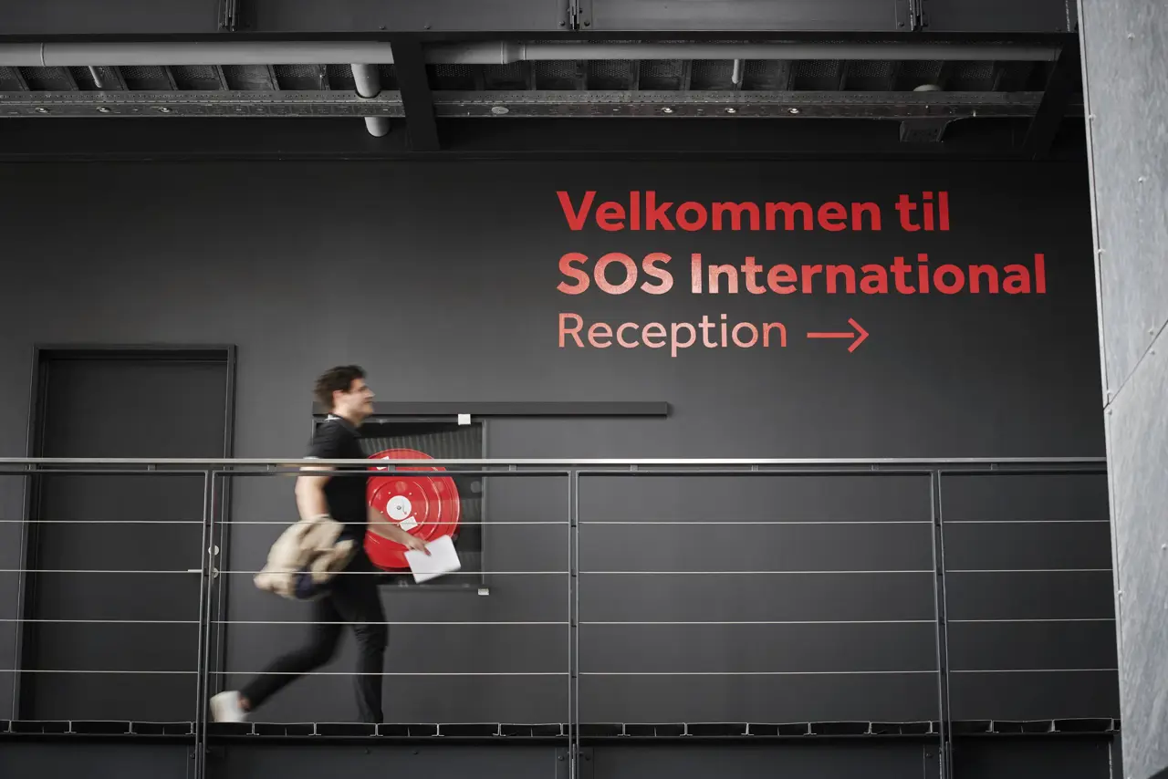 Man går snabbt förbi en logotyp på en svart vägg.