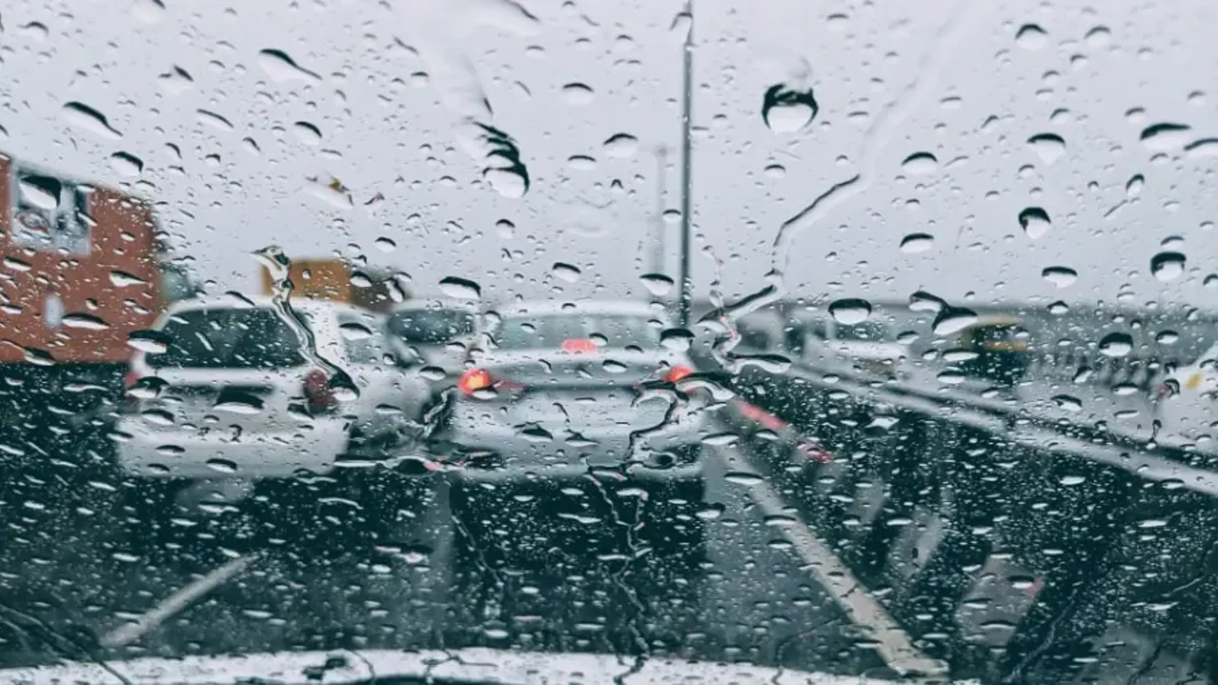Bild tagen inifrån framrutan på en bil. Regn och droppar försämrar synen ut från bilen som sitter fast i en bilkö på en motorväg.