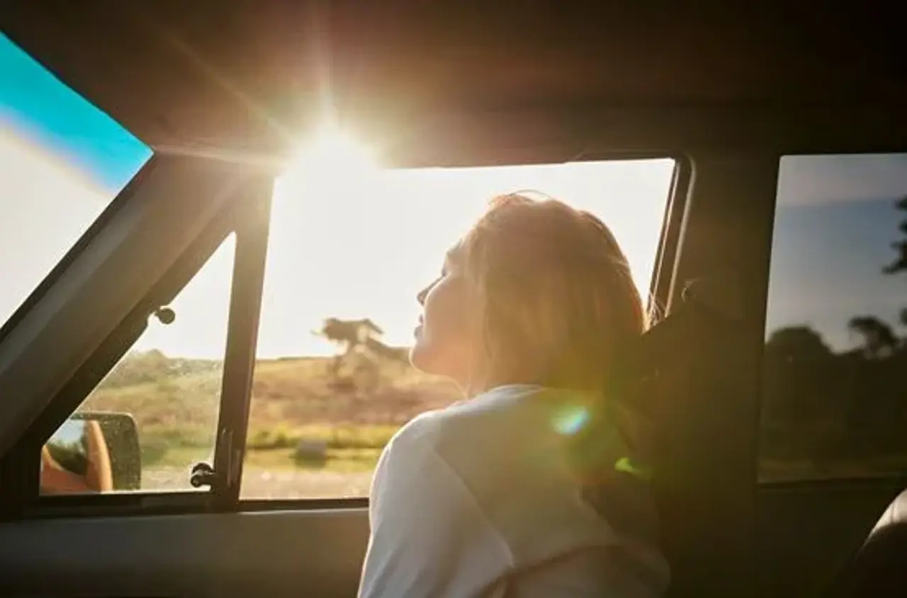 Dame kigger ud af bilvindue. Solen skinner. 