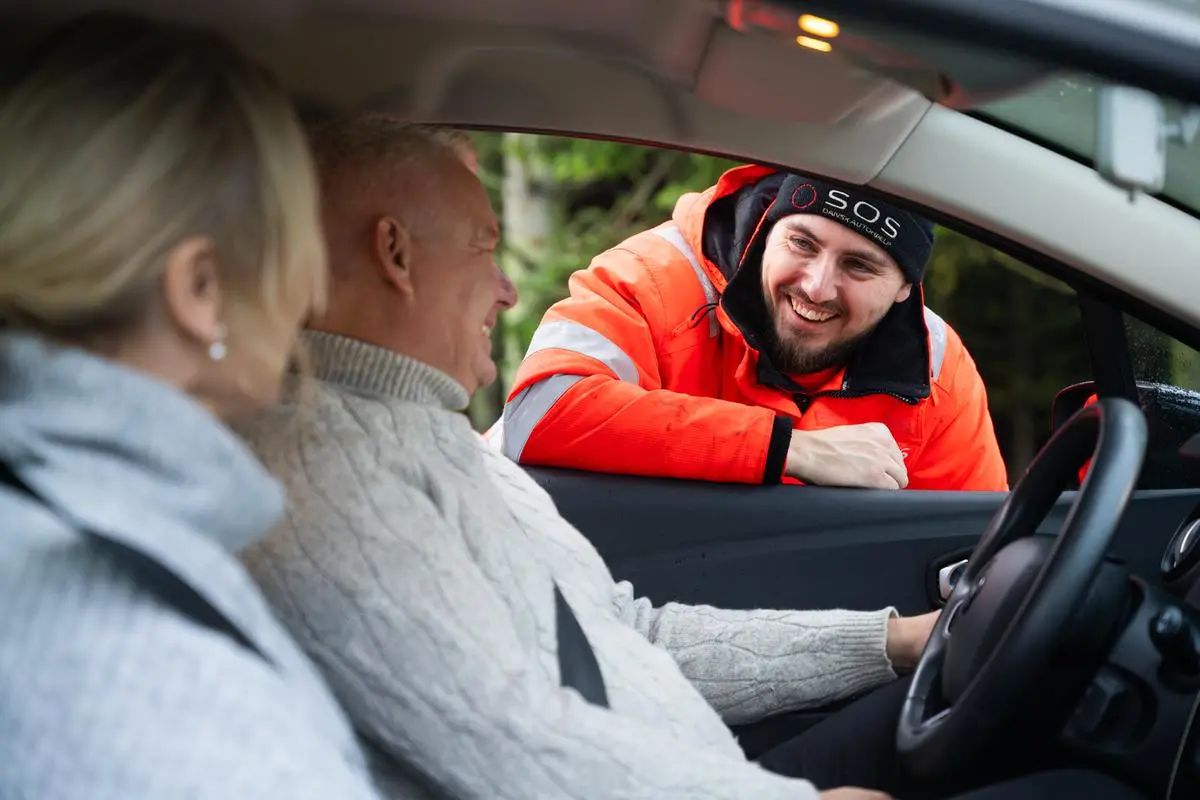 Par sidder i bil. Autoredder står i bilvinduet og taler