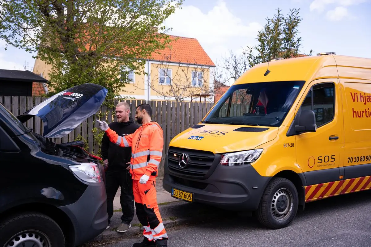 Autoredder står og taler med en kunde og kigger ned i motoren på en bil