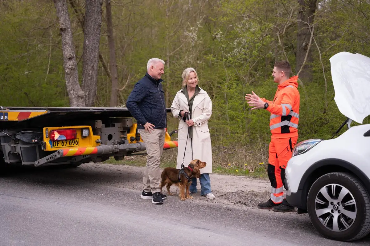 Par står og taler med autoredder ved bil, med motorhjelm oppe