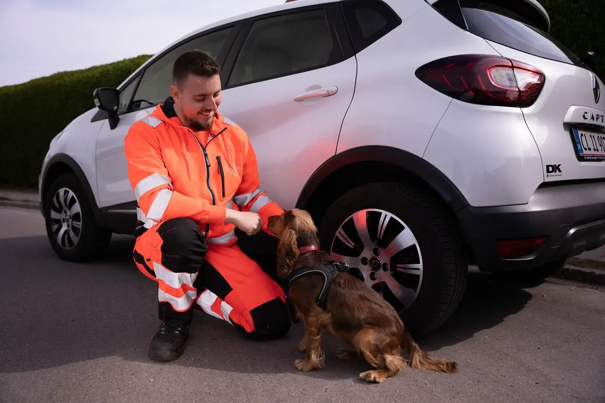 Autoredder sidder på huk og snakker med en hund