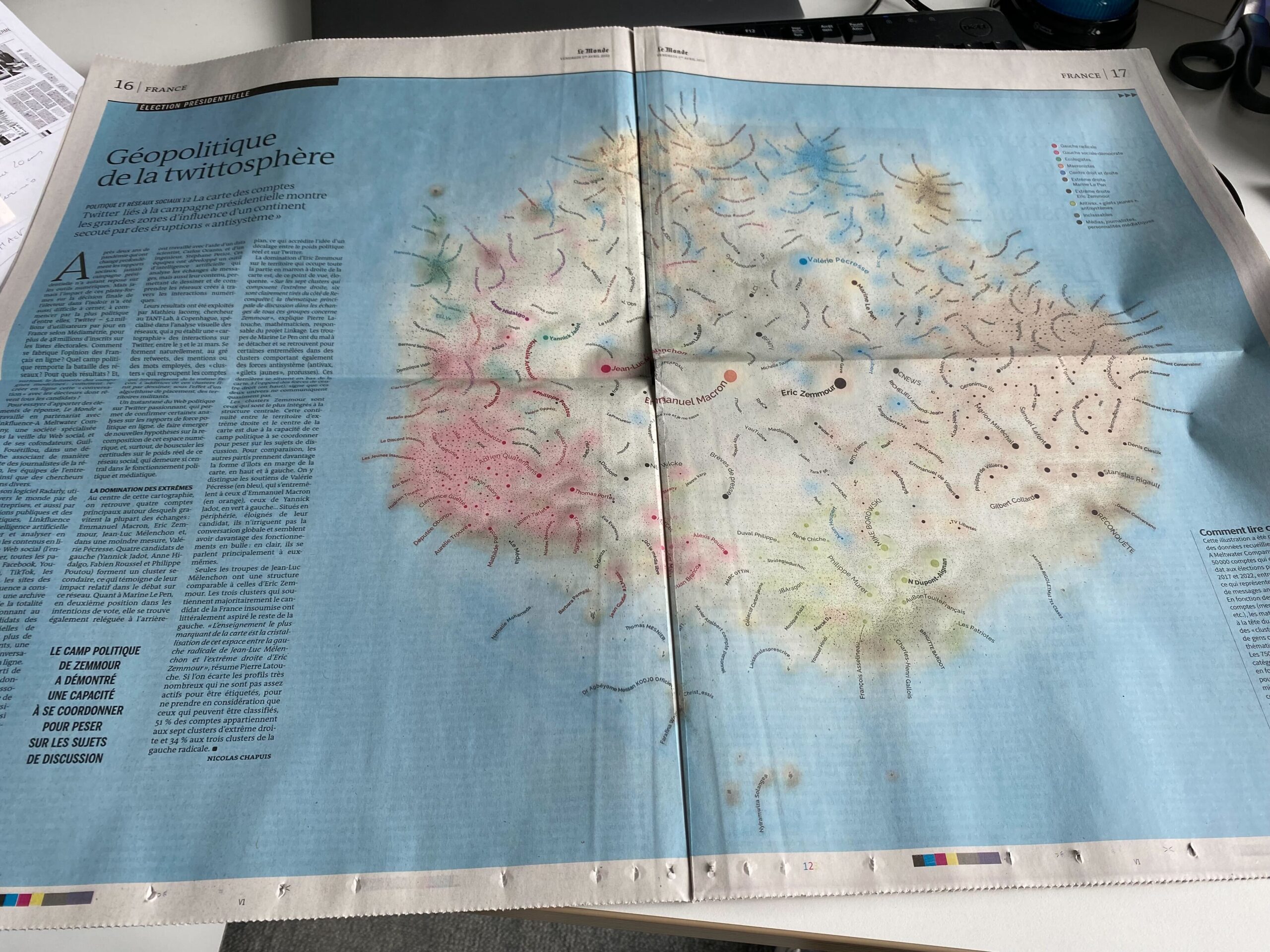 A photo of a Le Monde newspaper on a table, open on a page with a blue background and a complex network with curly text labels. The title is "Géopolitique de la twittosphère" but most of the text is hard to read.