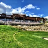 A view of the clubhouse at Black Mountain Golf Club in Kelowna, with manicured greens, flowering plants, and a blue sky.