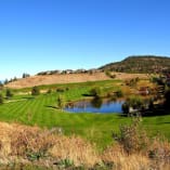 Wide view of Gallagher's Canyon Pinnacle Course in Kelowna featuring green fairways, a pond, and surrounding hills.