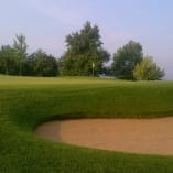 a view of a golf course with a sand trap in the foreground and trees in the background