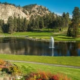 a golf course with a pond and a fountain in the middle of the grass and a mountain in the background