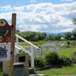 A sign in front of a grassy area with a wooden post displaying Michealbrook Golf Course information and a Jenish House Design Limited logo, located in Kelowna.