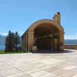 Wine barrels outside an archway structure at Mission Hill Family Estate Winery in West Kelowna, overlooking a scenic landscape and lake.
