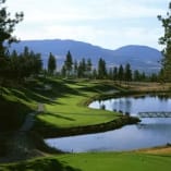 a view of a golf course with a lake and bridge in the foreground and mountains in the background