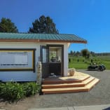 a small white building sitting on top of a lush green field next to a motorcycle parked on the side of a road at Orchard Greens Golf Club in Kelowna