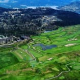 an aerial view of a golf course with a lake and mountains in the background and a city in the distance at Predator Ridge Golf Resort in Vernon