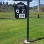 A sign for hole 6 at Spallumcheen Golf & Country Club in the middle of a green field with a blue sky and clouds in the background.