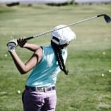 A person in a blue sleeveless shirt and purple shorts practicing golf swings at The Golf Centre Practice Facility in Kelowna.