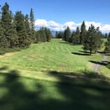 a view of a golf course from the top of a hill in the distance is a road and trees at The Harvest Golf Club in Kelowna.