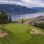 A view of a golf course with a lake and mountains in the background of the picture.