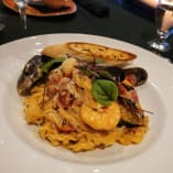 a plate of pasta with mussels and a glass of wine on a table with a lit candle in the background