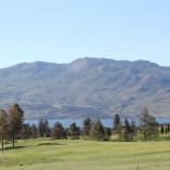 A scenic view of Two Eagles Golf Course in West Kelowna with mountains and a lake in the background.