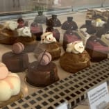 A display case filled with various types of cakes and desserts on top of a metal shelf.
