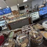 a bakery filled with lots of different types of breads and pastries in plastic containers on top of a wooden table