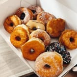 a box filled with lots of doughnuts on top of a wooden table next to a cup of coffee