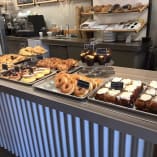 A counter filled with lots of different types of doughnuts on top of trays next to a metal radiator at 350 Bakehouse and Cafe in Kelowna.