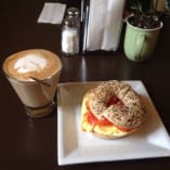 a bagel on a plate next to a cup of cappuccino and a drink on a table