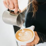 a person pouring a cup of coffee into a white cup with a white swirl on the top of it.