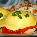 a white plate topped with two eggs benedicts next to a side of rice and vegetables on a table