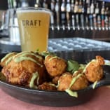 a bowl filled with fried food next to a glass of beer on a bar top with a pint of beer in the background