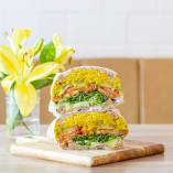 a cut in half sandwich sitting on top of a wooden cutting board next to a vase of yellow flowers