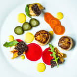 a white plate topped with different types of food on top of a white tablecloth covered in green olives, carrots, cucumbers, and other vegetables.