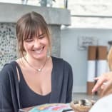 Two women are talking to each other at a table with a cake on it and a cupcake in front of them at Bliss Yoga Lounge, Kelowna.