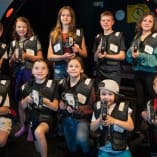 A group of children at EnergyPlex Entertainment Centre in Kelowna, holding laser tag equipment, smiling at the camera.